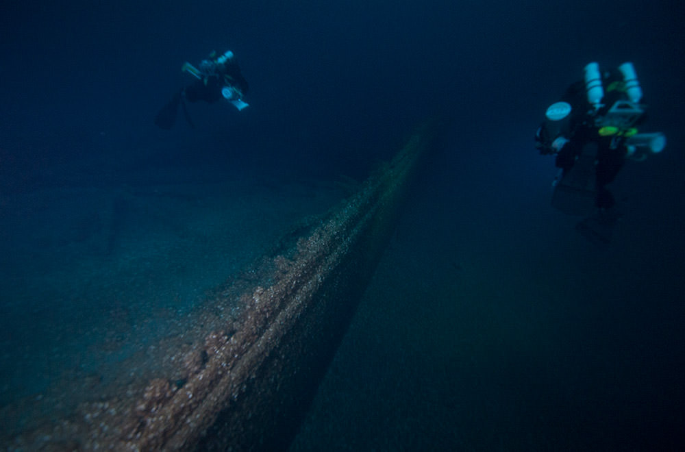 Two technical divers swim alongside the hull of the Egyptian