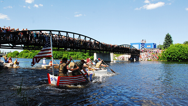 People paddling cardboard boats as a crowd watches