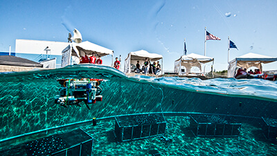 an rov is piloted just below the surface in a pool as people look on from the deck