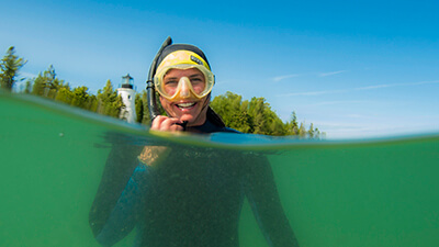 A snorkeler smiles with a lighthouse in the background