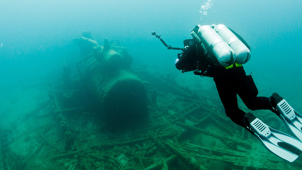 a diver swims towards machine-looking debris from a shipwreck