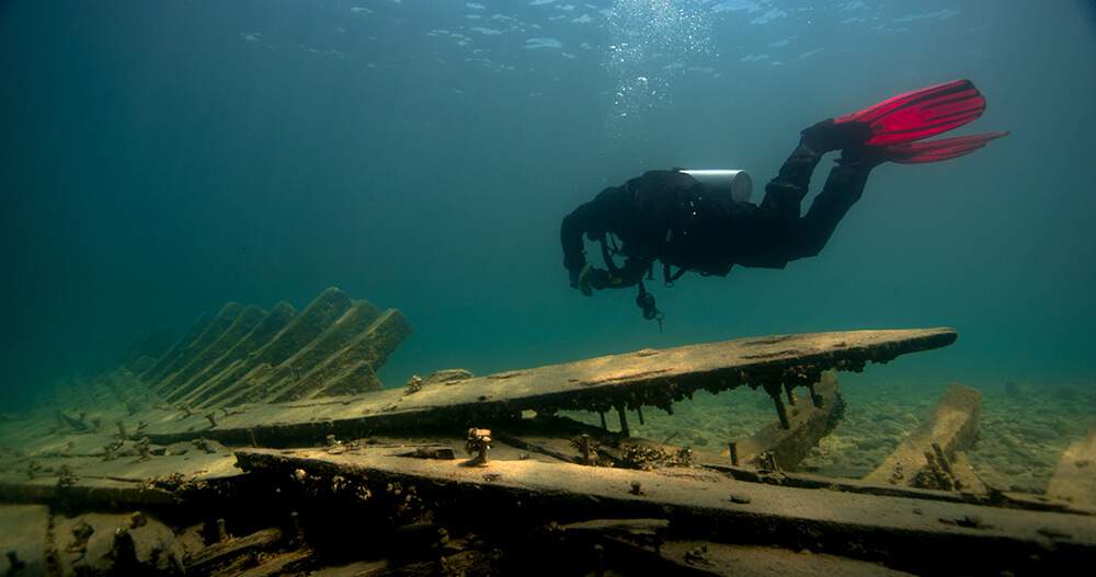 a diver with red flippers swims above a shipwreck