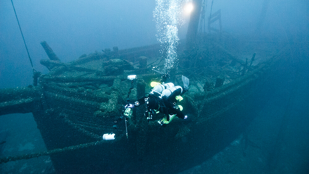 a diver swims in front of a wooden shipwreck