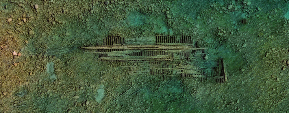 an overhead shot of water shows a shipwreck just below the surface