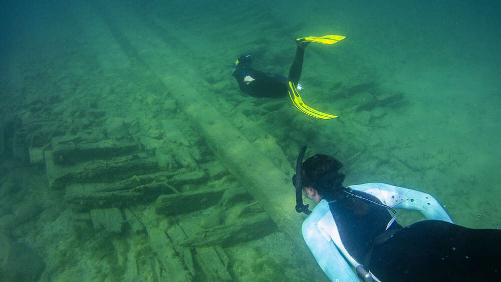 Two snorkellers swim above a wooden shipwreck