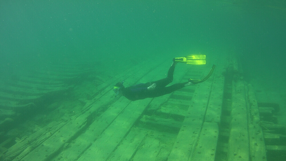 A snorkeller swims examines a wooden shipwreck
