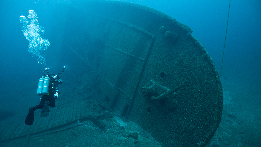 A diver swims towards a large shipwreck resting on its side