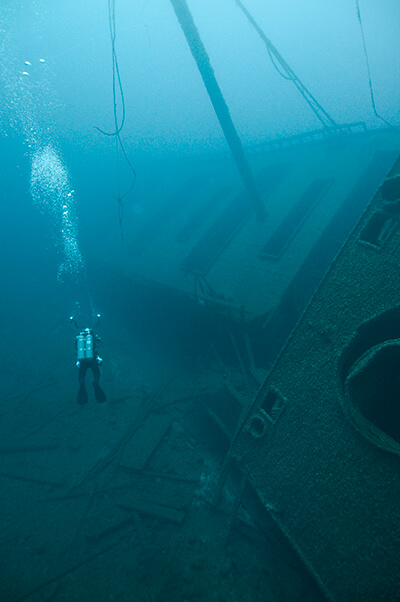 A diver swims next to a shipwreck restoiing on its side