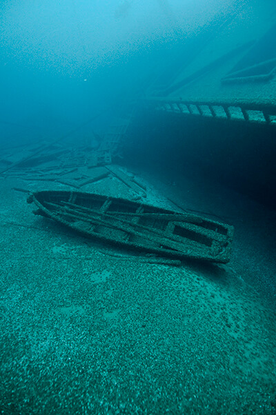 A small row boat rests next to a much larger shipwreck