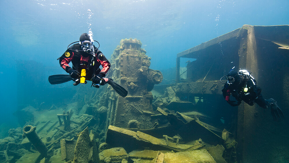 Divers swim past heaps of metal from a shipwreck