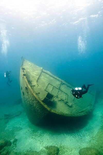 Two divers swim around the bow of a shipwreck