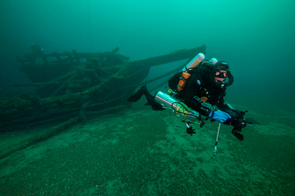 a diver holds a camera with a shipwreck in the background
