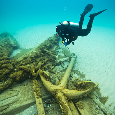 A diver floats above an anchor and wood debris