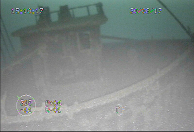 a grainy underwater shot of a shipwreck showing a boxy structure with windows