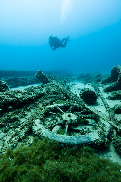 a diver swims above a wheel and other debris from a shipwreck