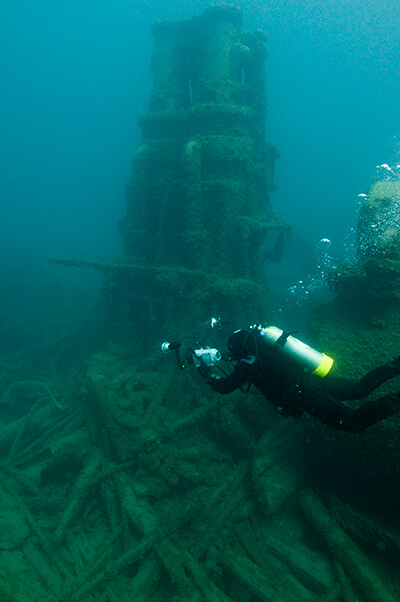 A diver swims near a pillar-like structure from a  shipwreck