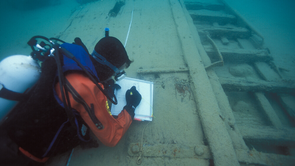 a diver takes measurements of a shipwreck