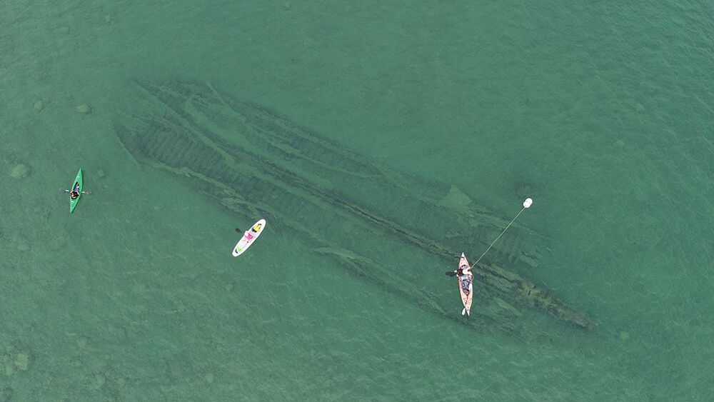 Paddleboarders float above a shipwreck visible form the surface