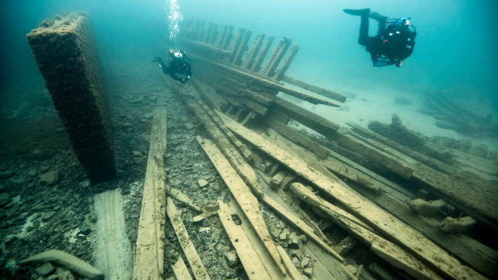 Two divers swim over loose wood planks of a shipwreck