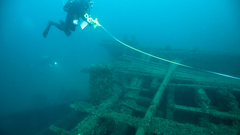 A diver takes measurements of a shipwreck