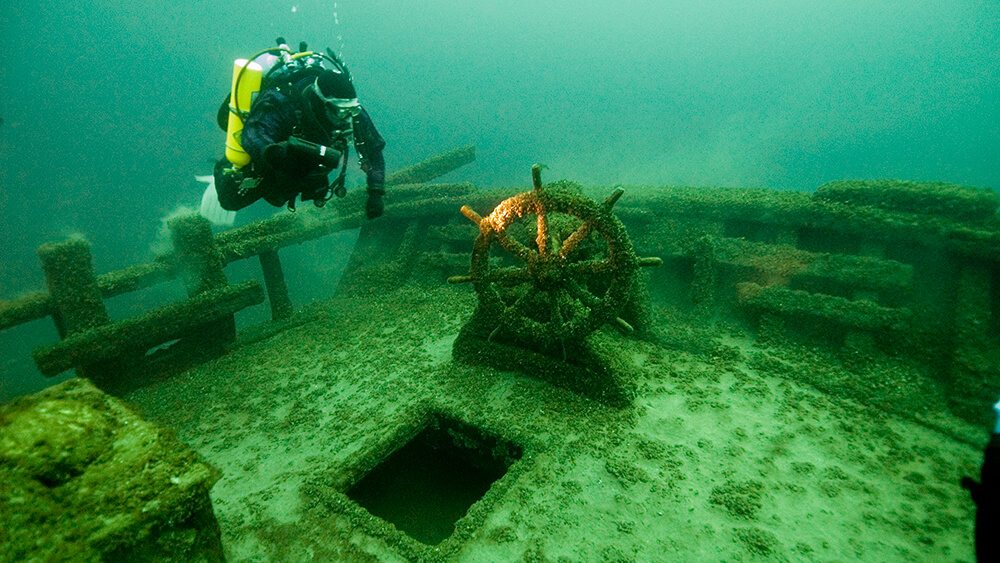 A diver swims next to the wheel of a shipwreck