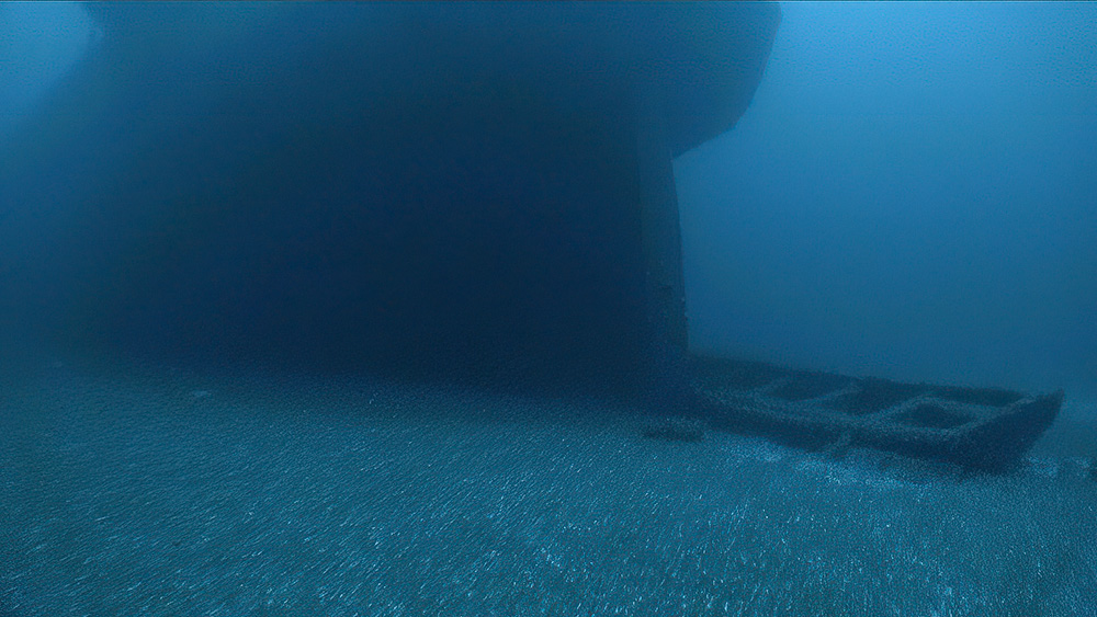 A lifeboat sits on the seafloor next to a much larger sunken vessel